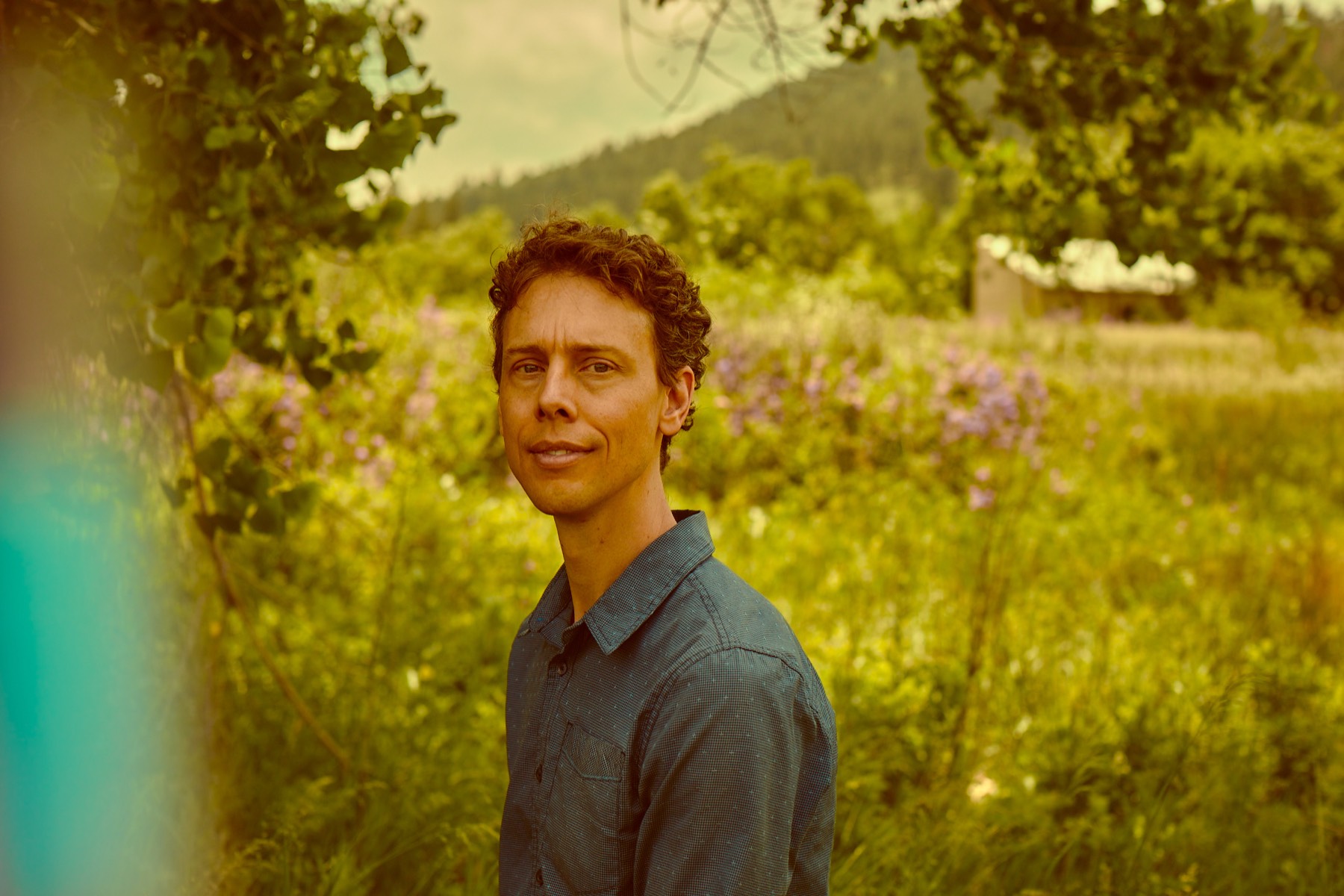 Mark Andreas standing calmly, framed by green foliage with a meadow behind