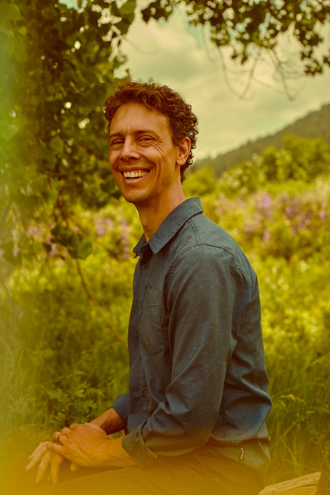 Mark Andreas, laughing, framed by trees in natural light.