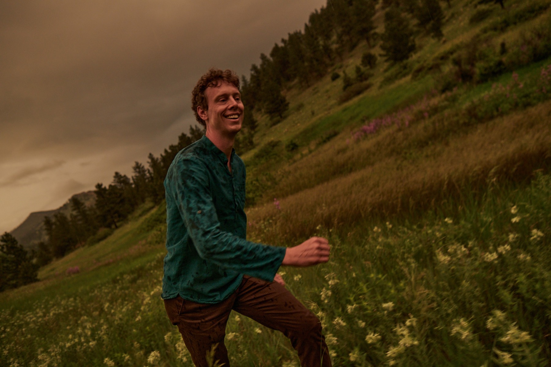 Mark Andreas mid-stride through a meadow beneath a dramatic stormy sky, smiling.