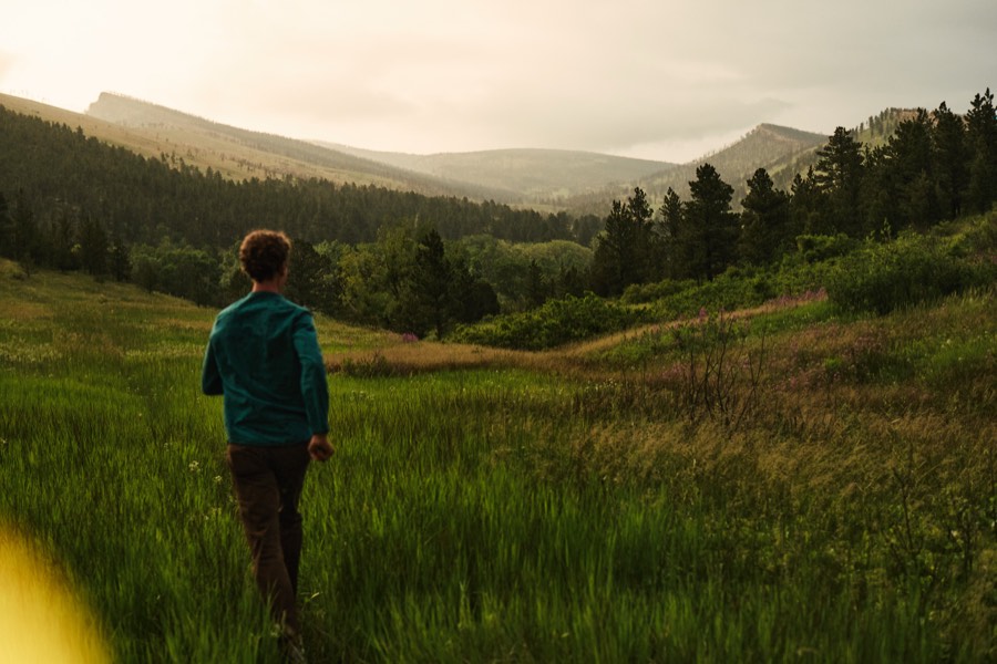 Mark Andreas walking through tall grass toward mountains at dusk