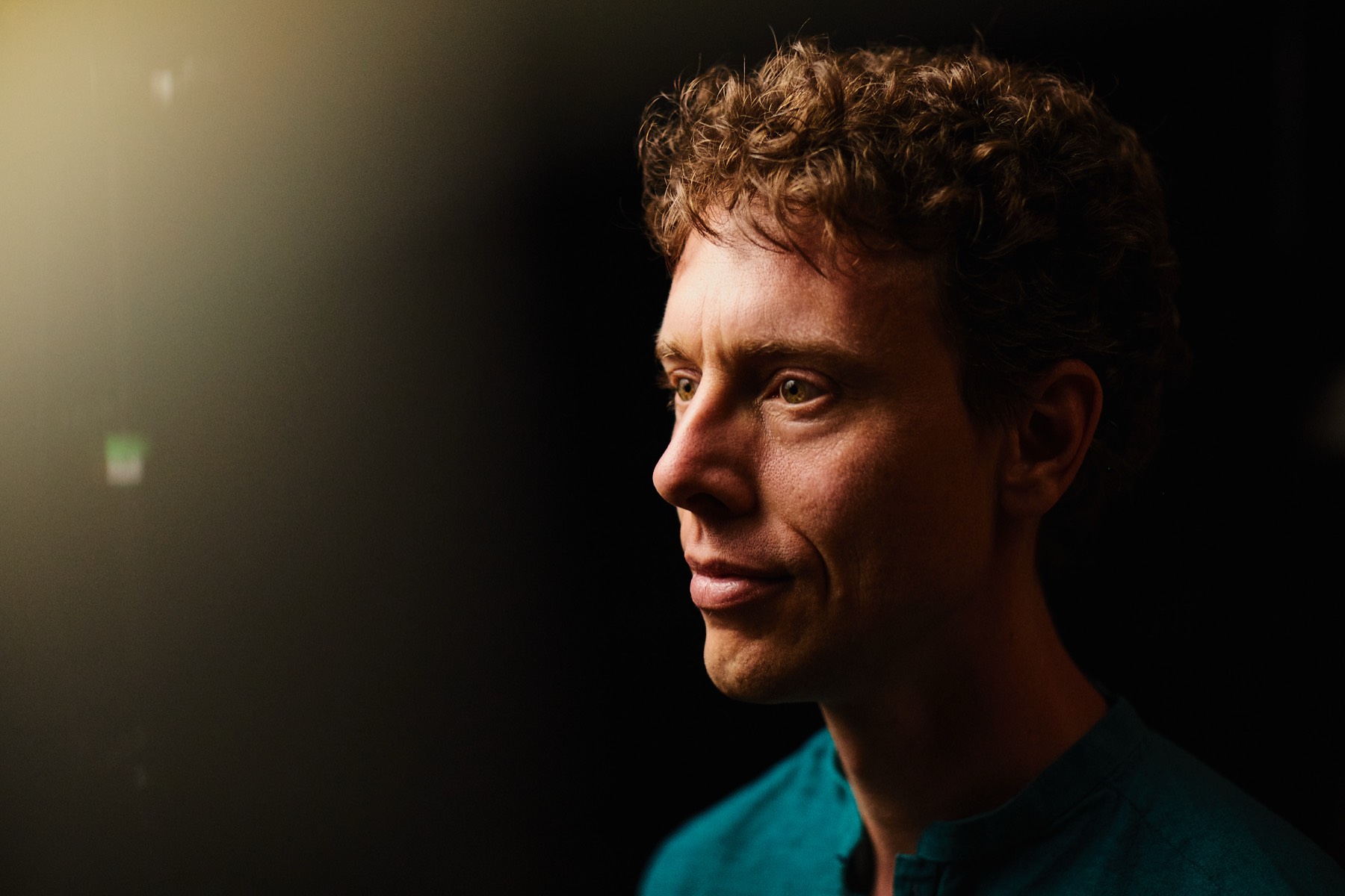 Close profile portrait of Mark Andreas, lit from the left against a near-black background.